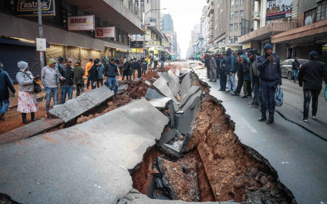 Commuters and pedestrians examine the damage to roads in the Johannesburg CBD after a gas explosion